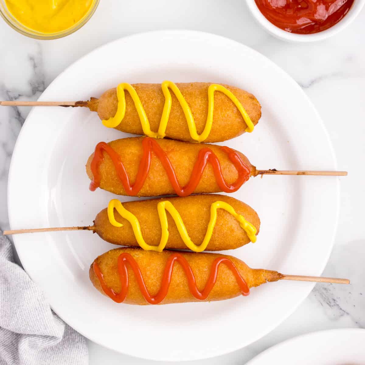 A plate of corn dogs with ketchup and mustard on them.