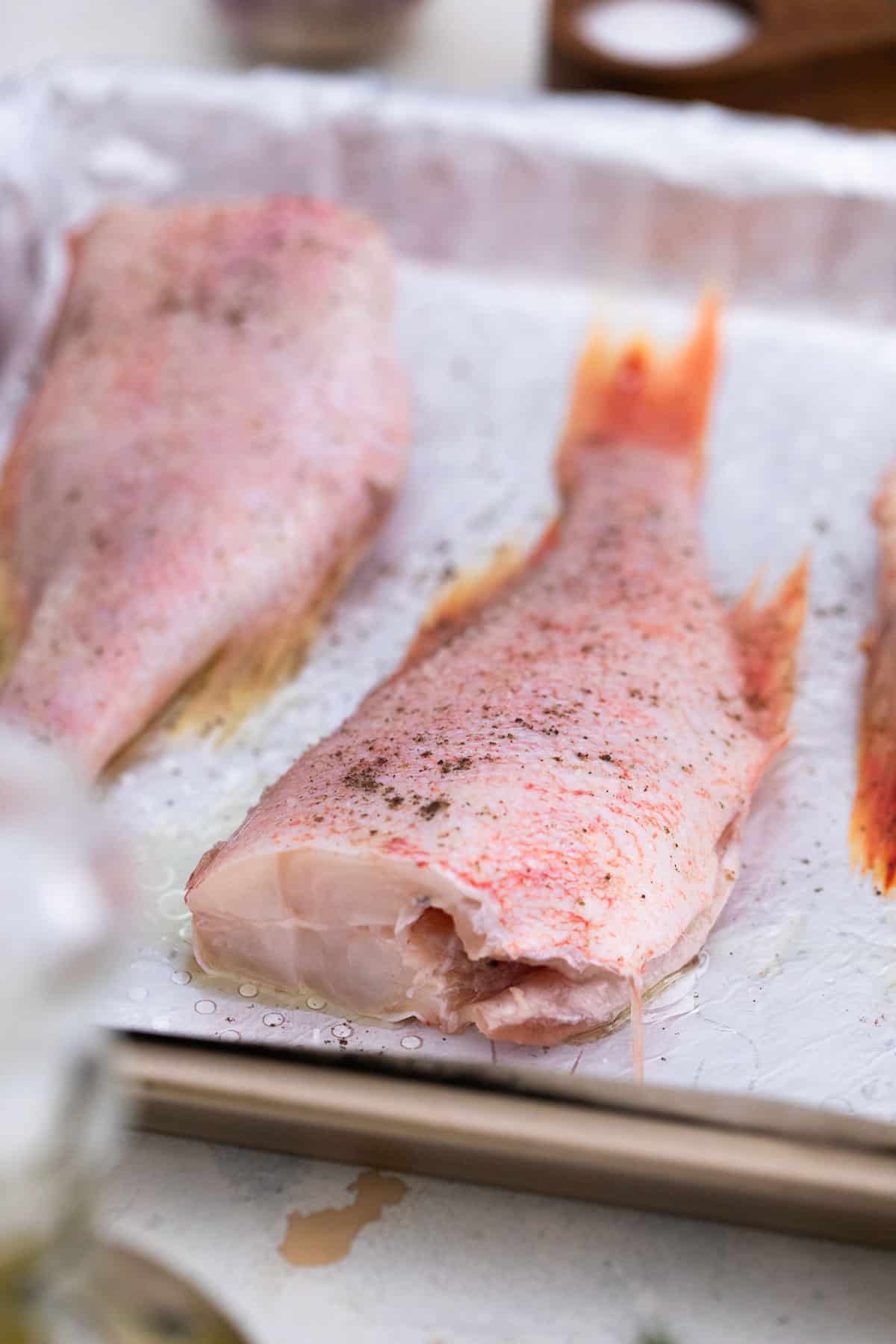 Some unbaked  fish on a baking sheet, seasoned with pepper.