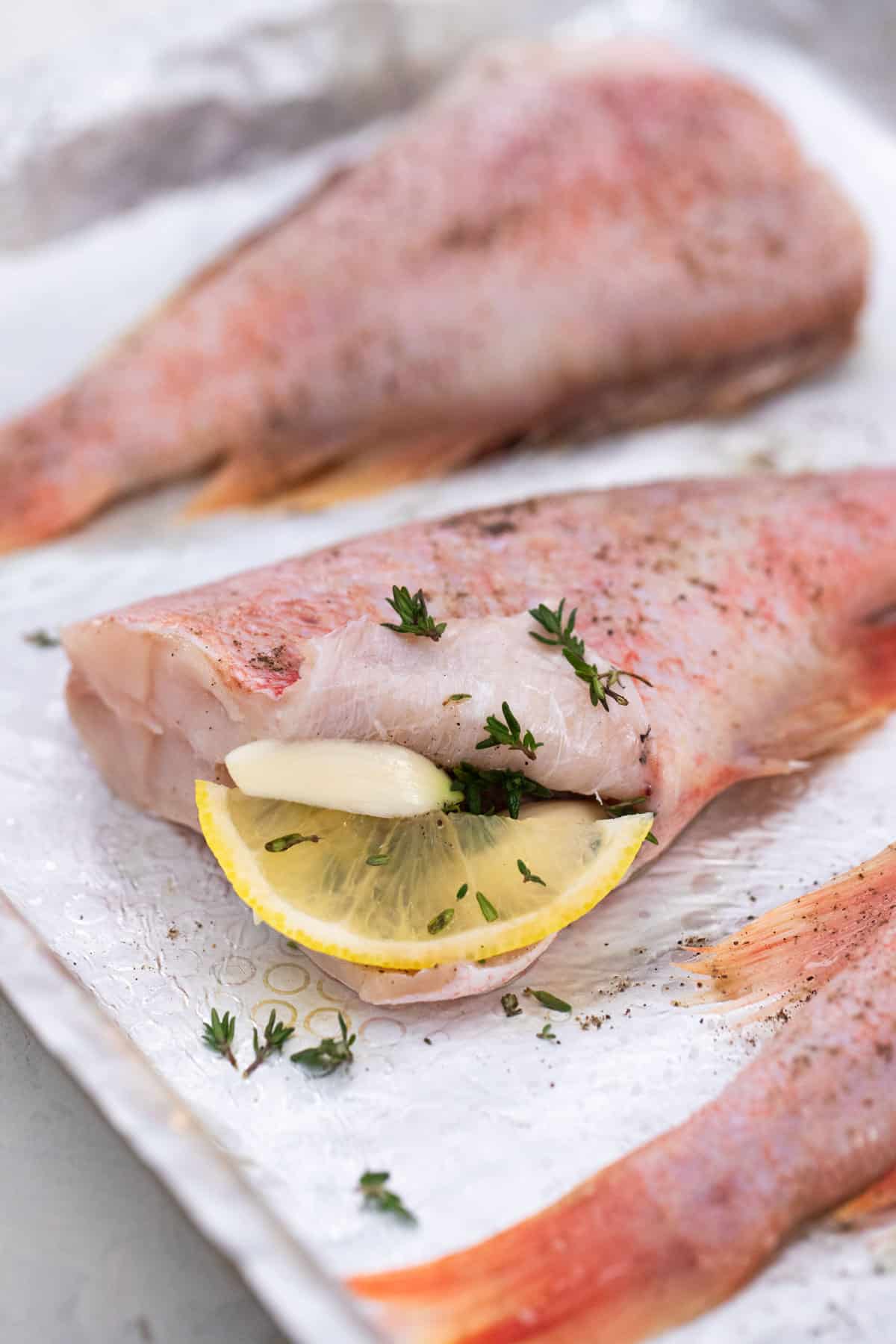 Seasoned, unbaked fish, on a baking pan and stuffed with lemon.