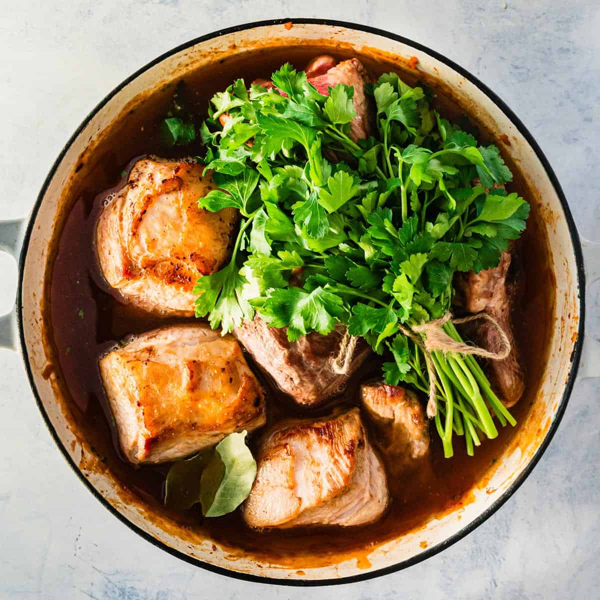 A pot of chunks of meat with a bunch of parsley.