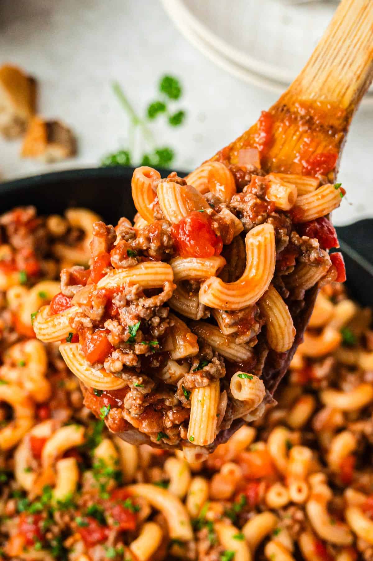 W wooden spoon with some elbow macaroni, ground beef, and tomato pieces on it.