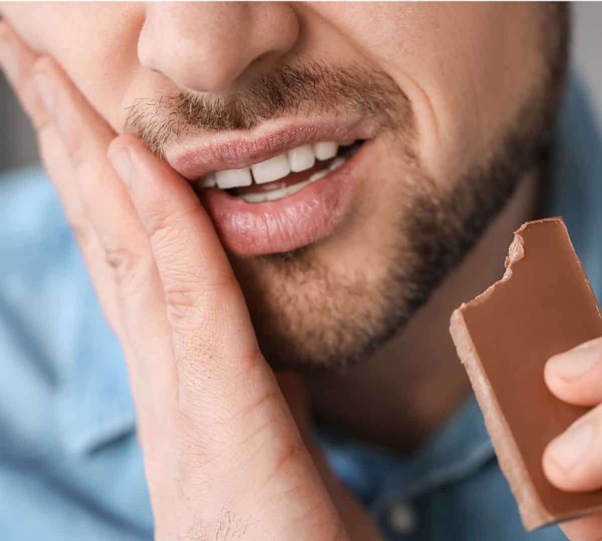 A man eating a chocolate bar with a painful grimace on his face.