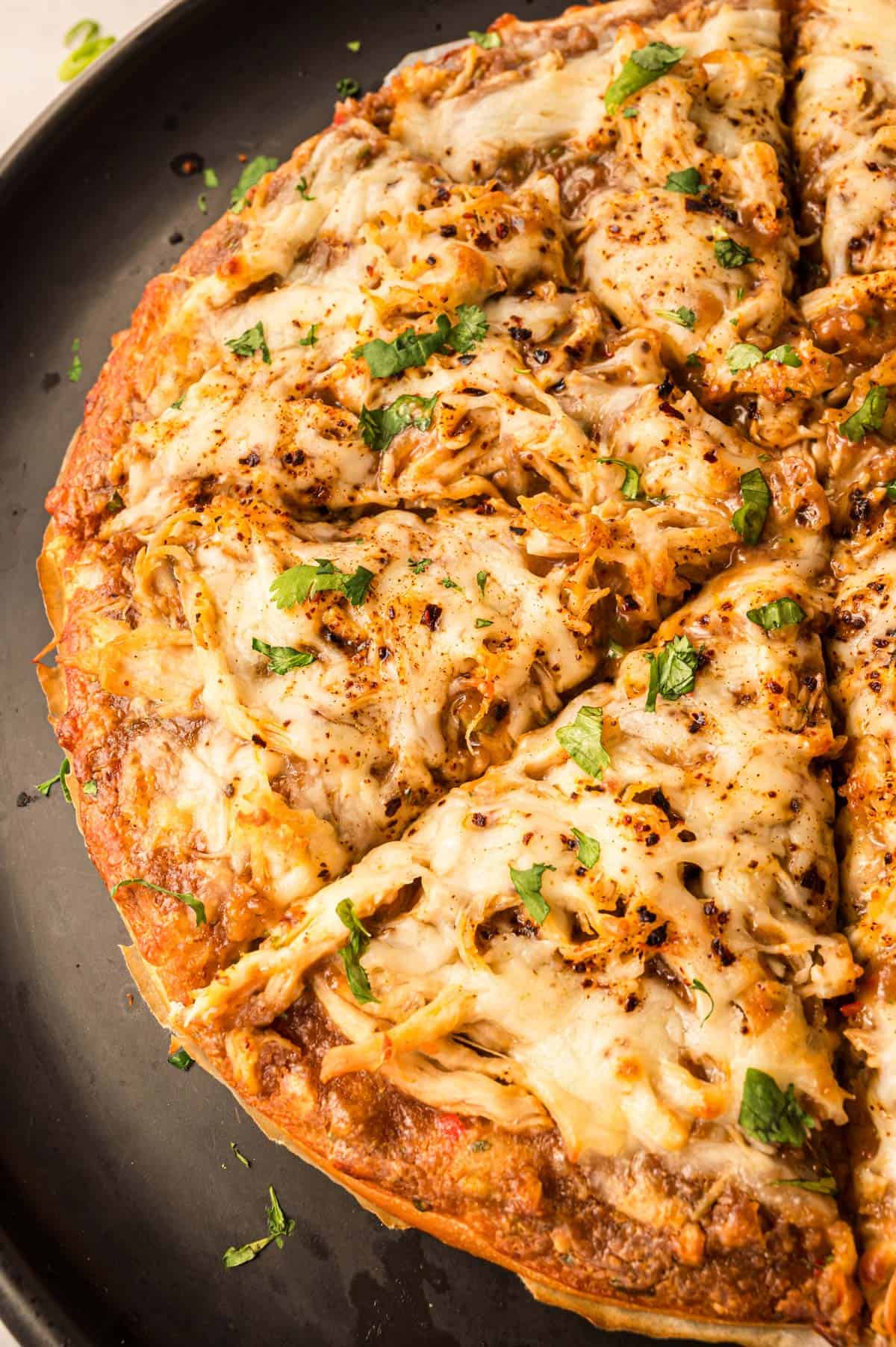 A sliced Thai chicken pizza on a pizza pan.