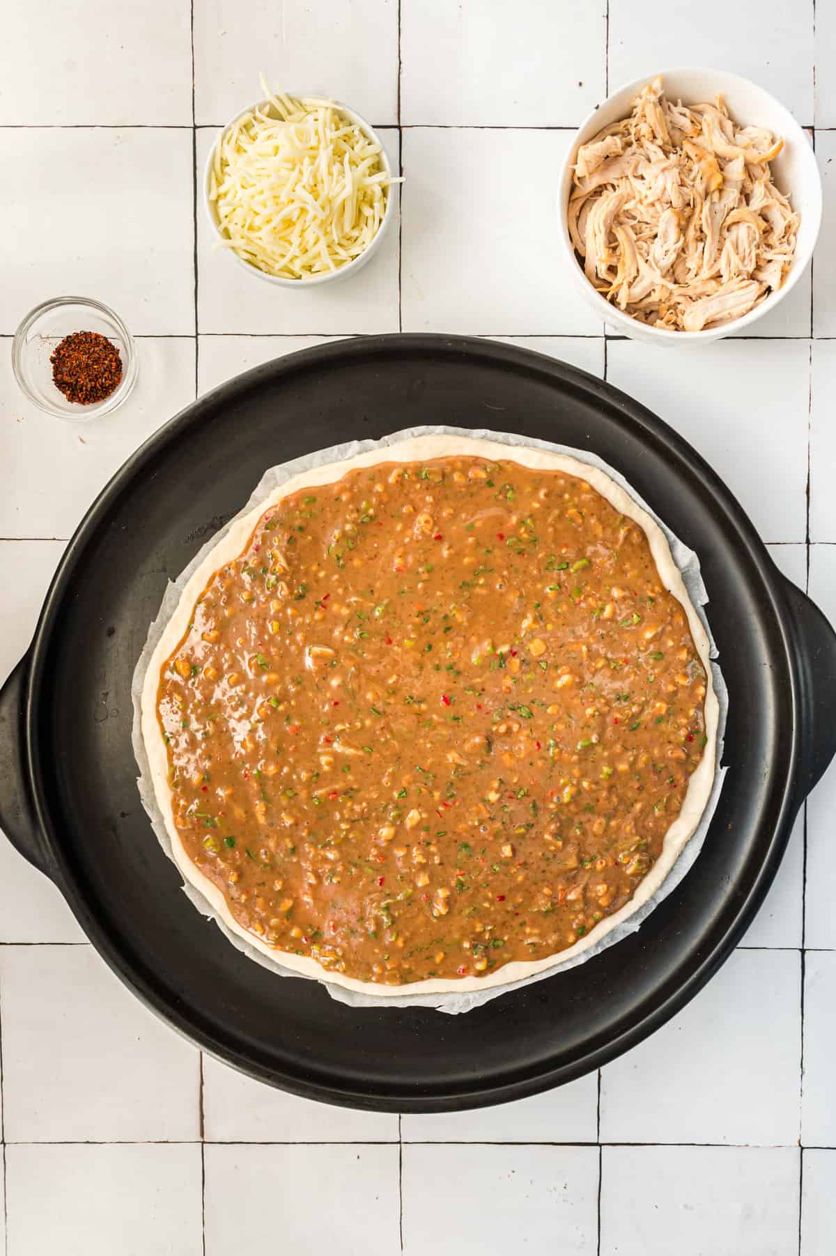 An unbaked pizza topped with peanut sauce.
