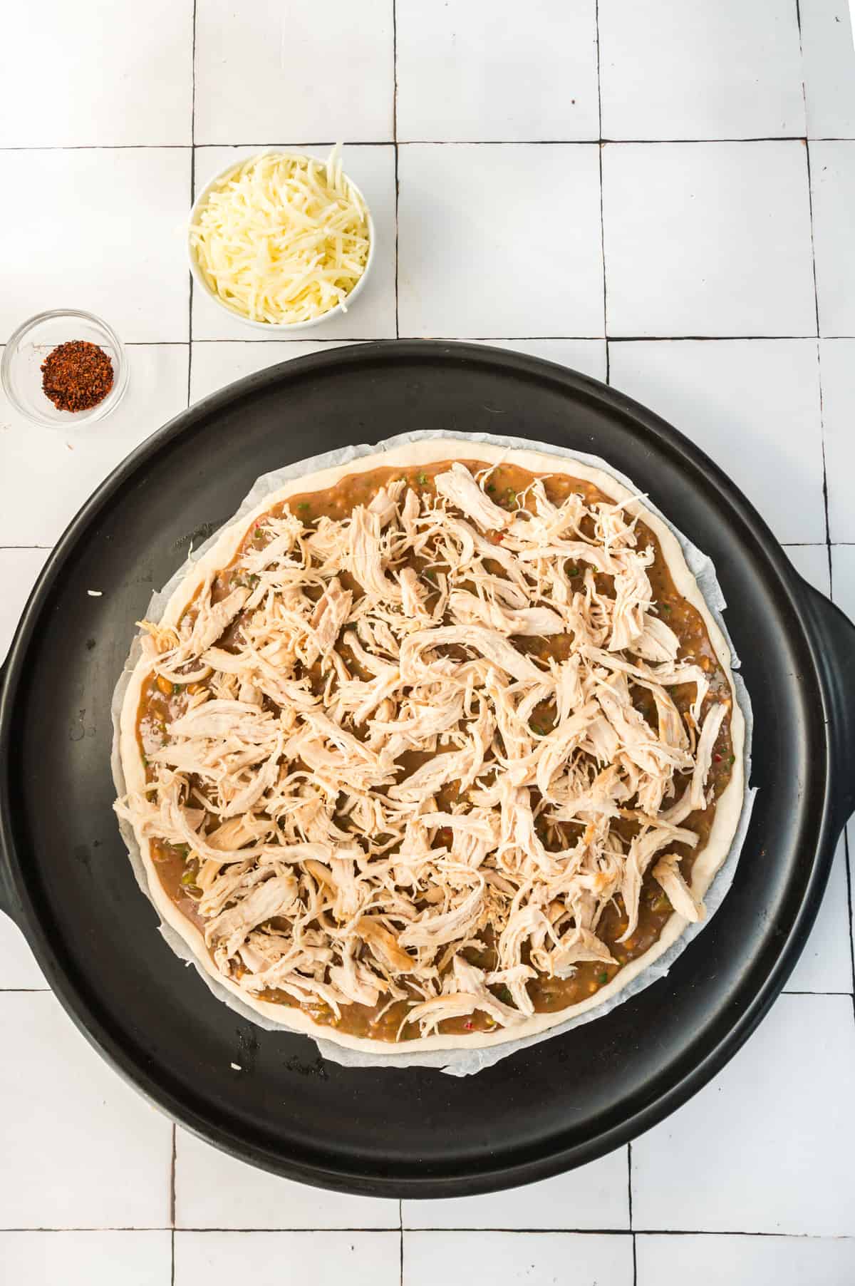 An unbaked pizza topped with shredded chicken.