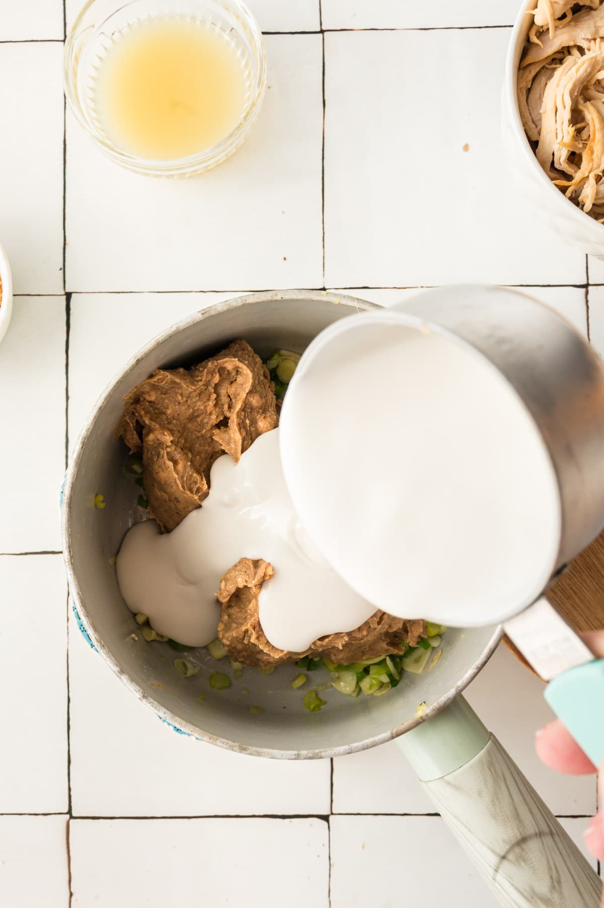 Adding coconut cream to a pan of peanut butter.