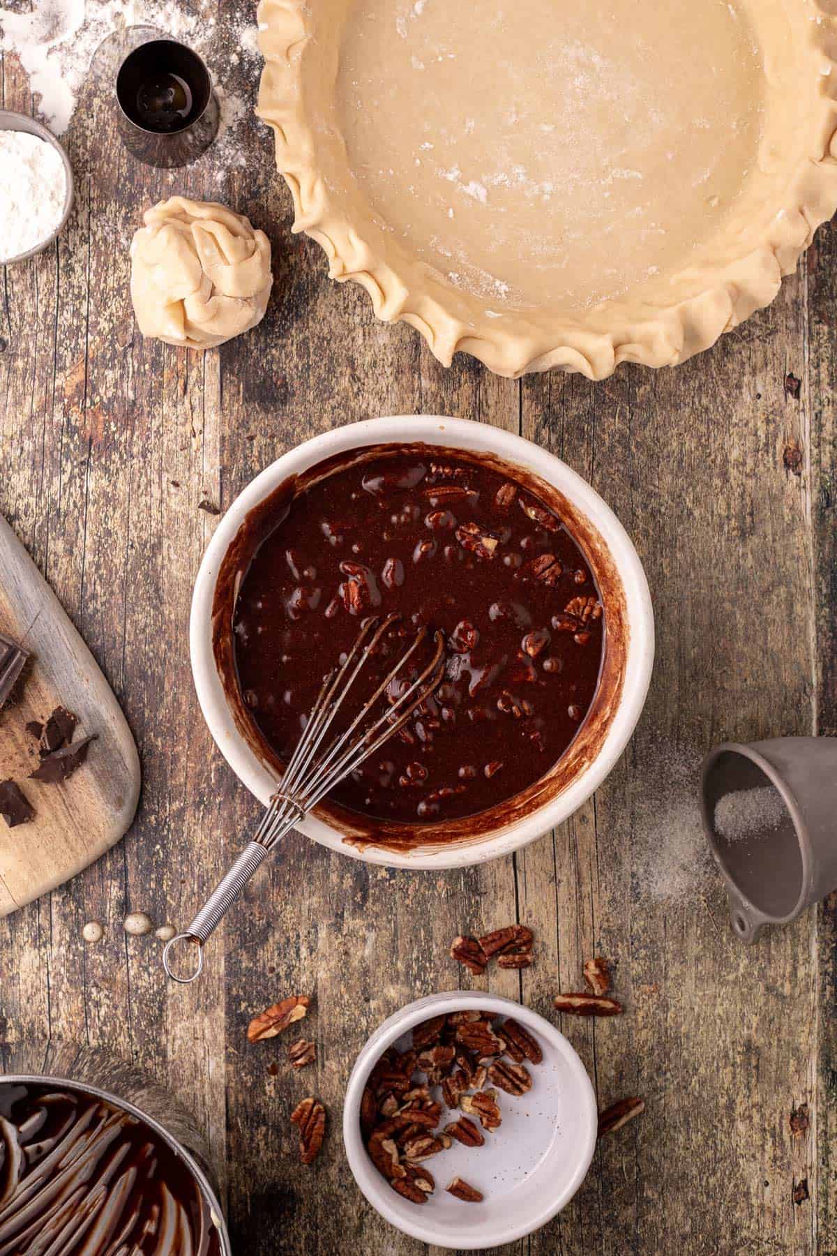 A mixing bowl with melted chocolate and pecans and a pie shell.
