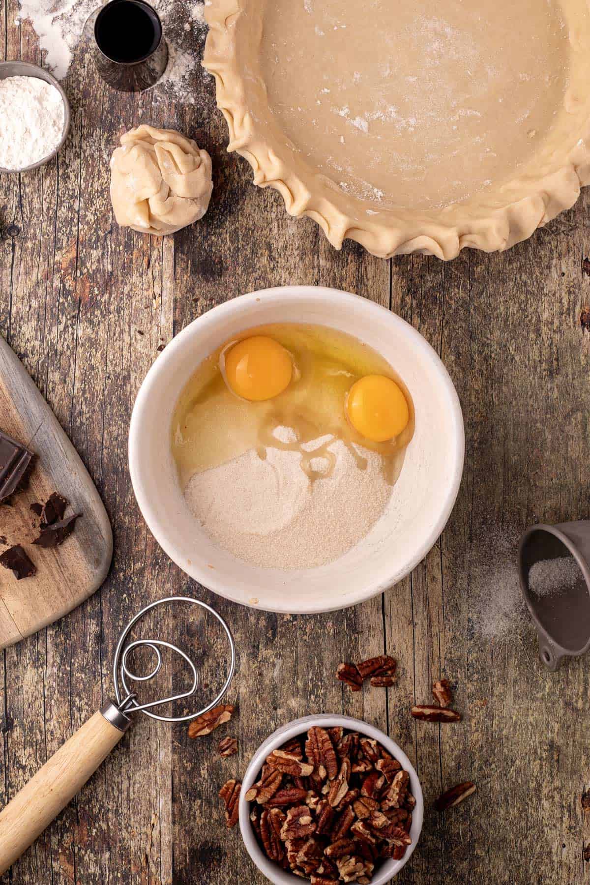 A mixing bowl with some eggs and a pie shell.