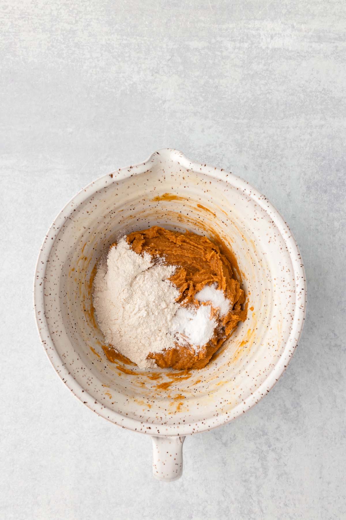 Some flour, baking soda, and salt, added to a mixing bowl of cookie dough.