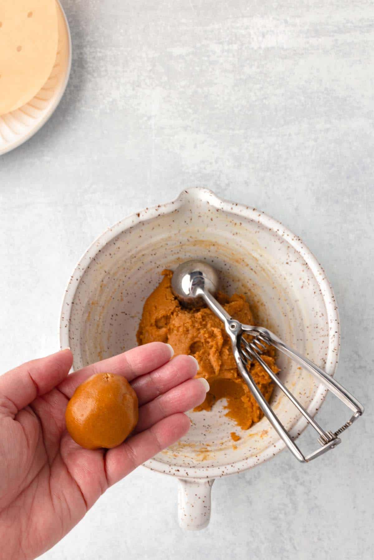 A small, rolled-up ball of cookie dough in someone's hand.