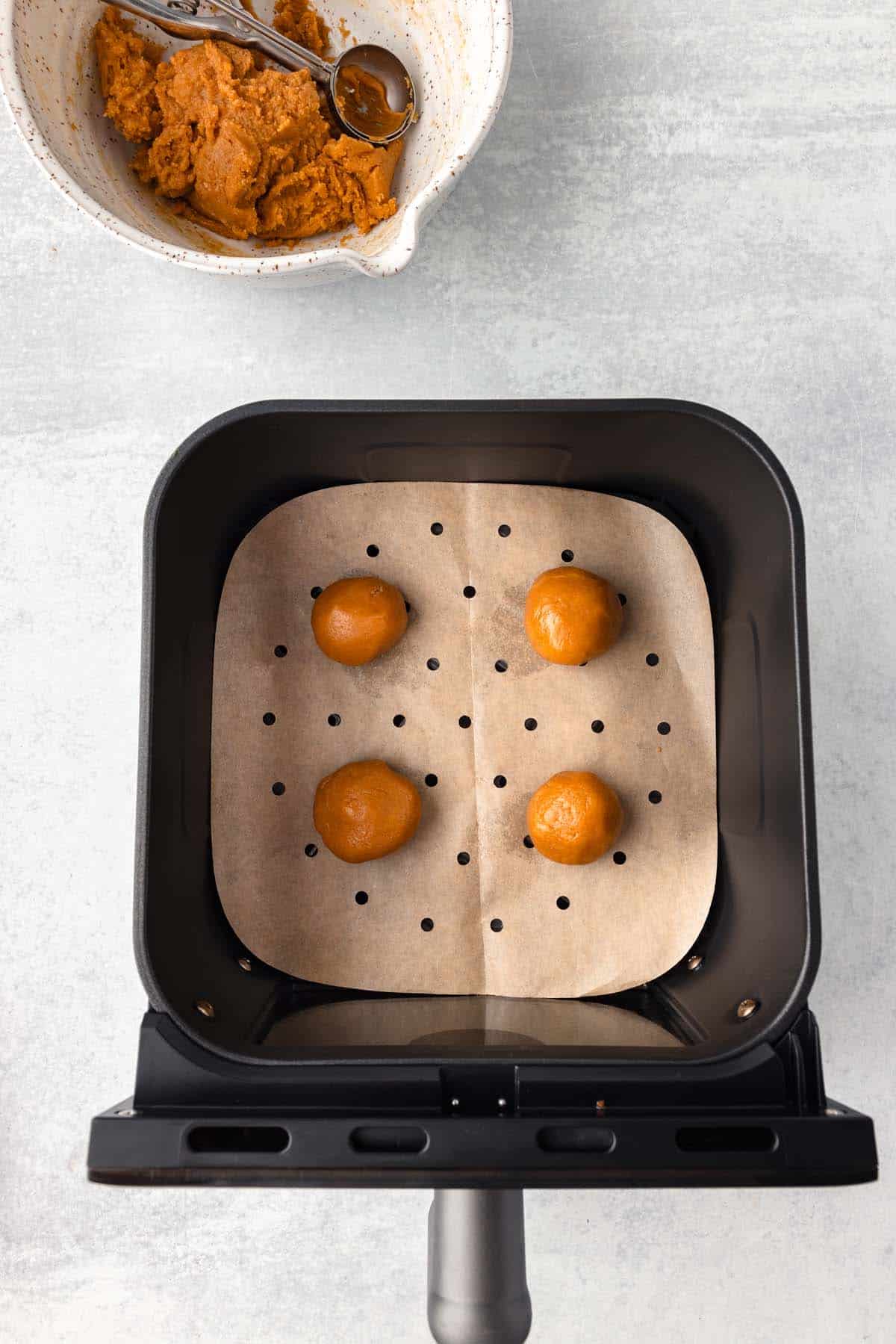 Four small balls of cookie dough in an air fryer basket lined with parchment paper.