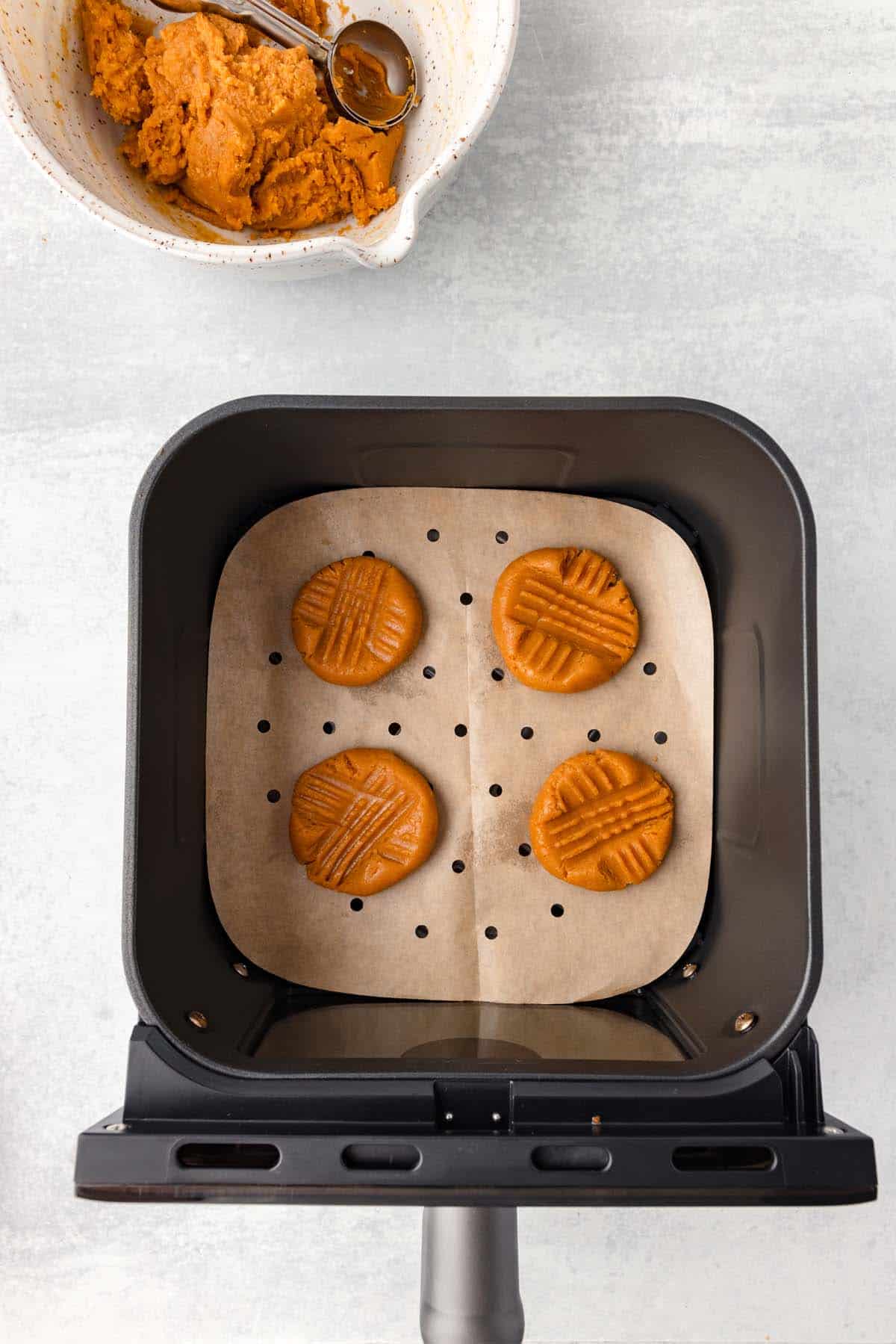 Some crosshatched unbaked cookie dough in an air fryer.