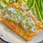 A plate of fish with tarter sauce on top, with green beans and salad.