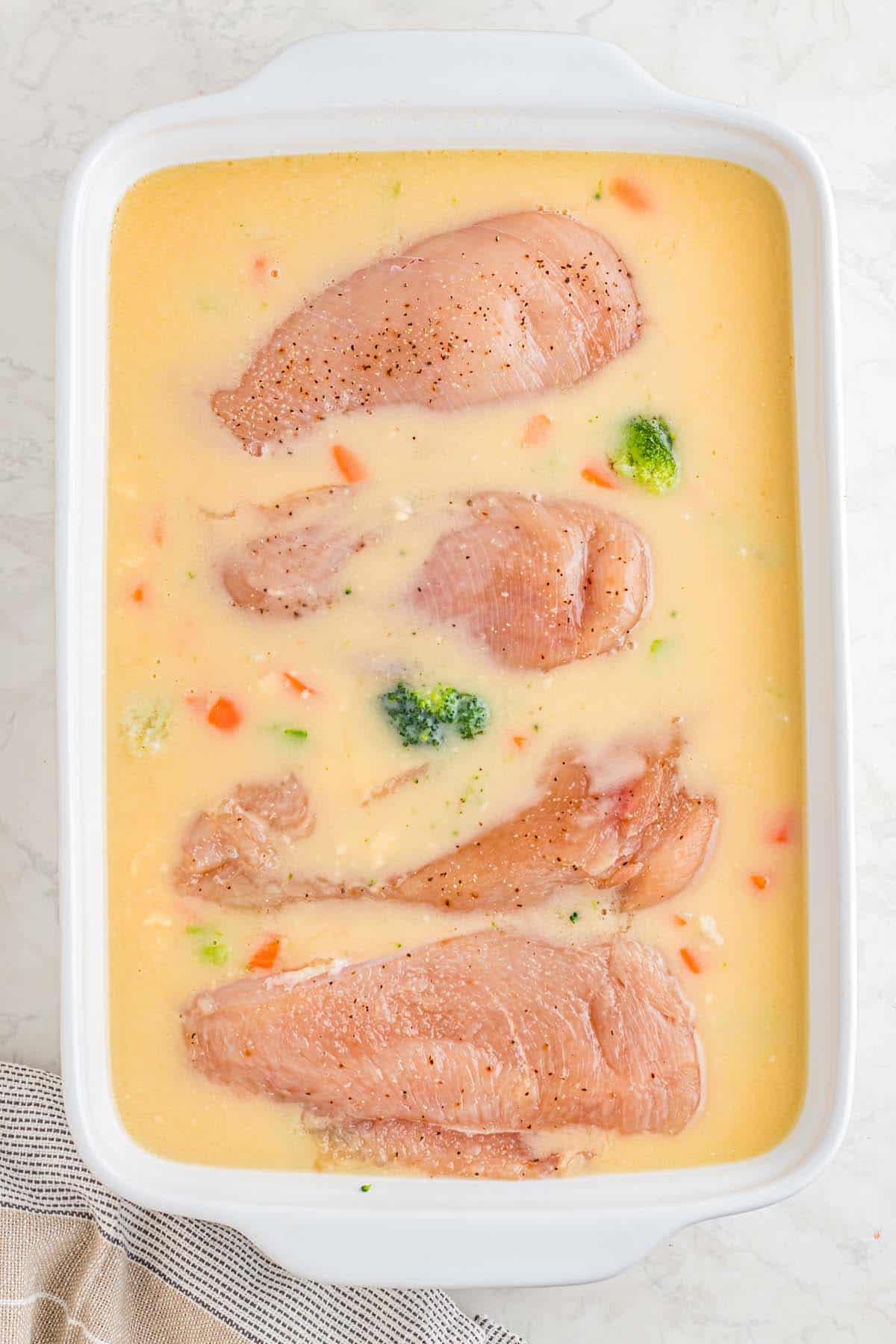 A casserole dish with chicken breasts in broth.