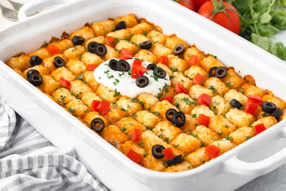 A tater tot casserole with sour cream, black olives, and chunks of tomato on top..
