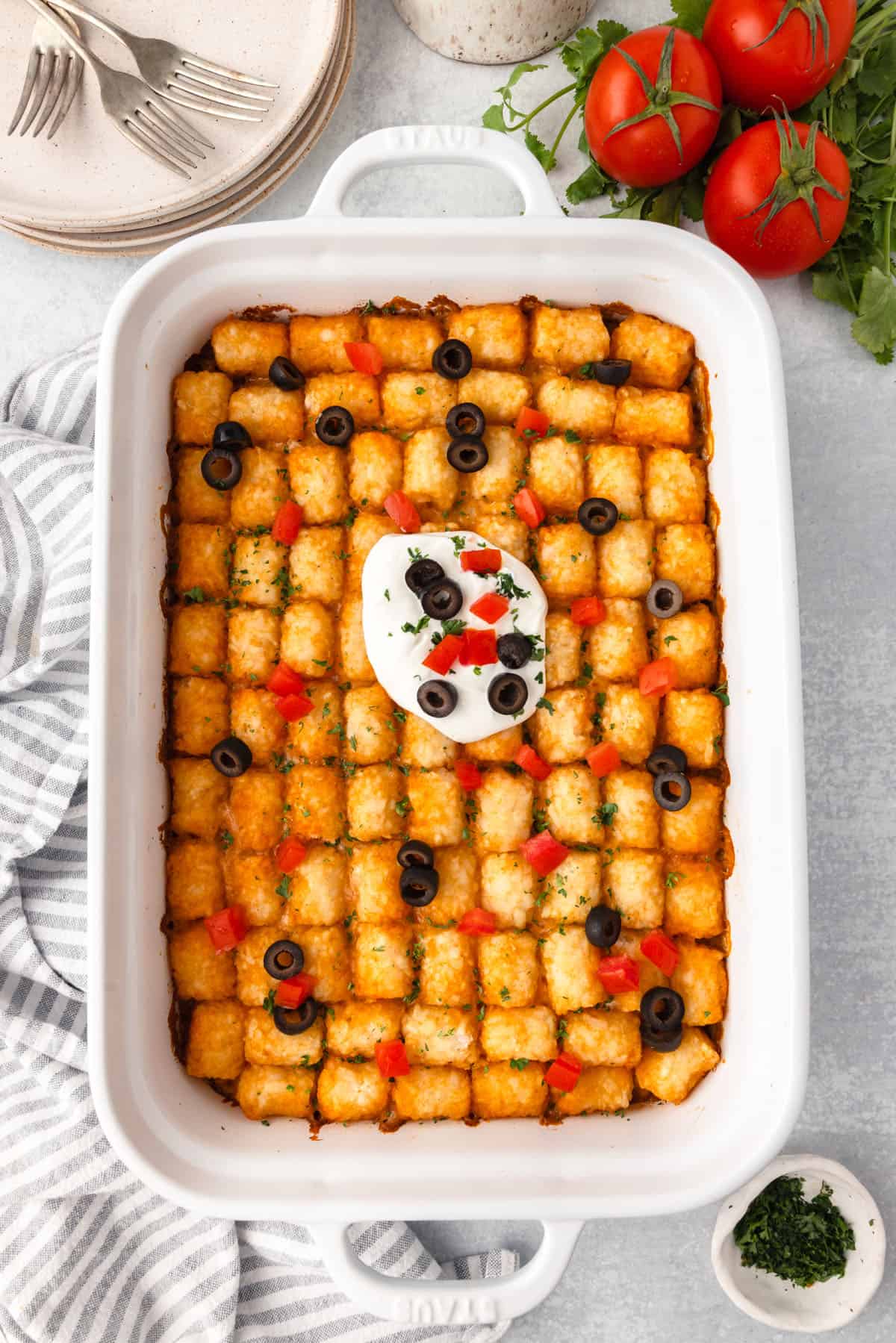 A baked tater tot casserole, topped with sour cream, diced tomatoes, and black olives.