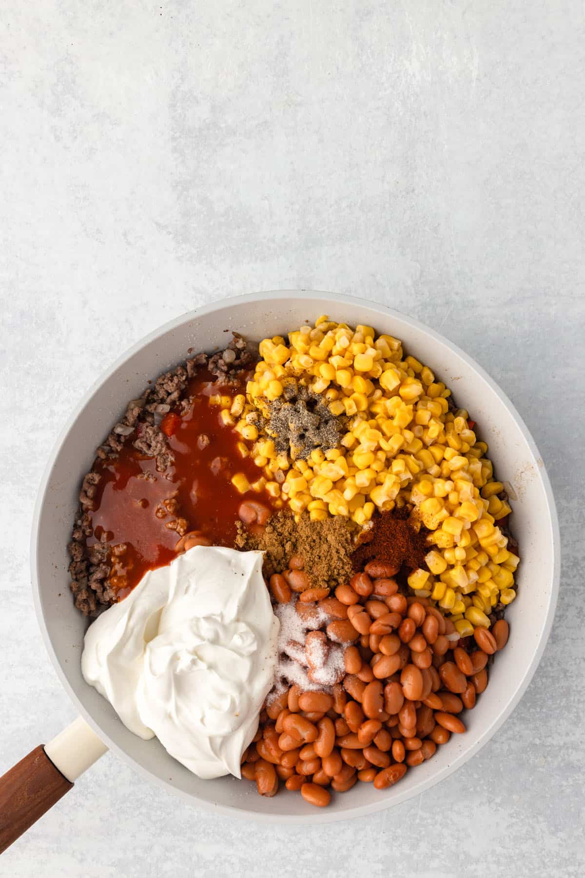 A bunch of corn and pinto beans in a skillet with browned beef and sour cream.