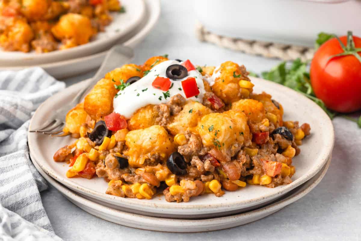 A plate of tater to casserole with tomatoes in the background.