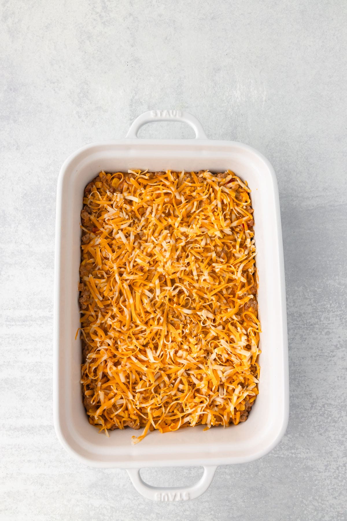 A casserole dish with shredded cheese spread on top.