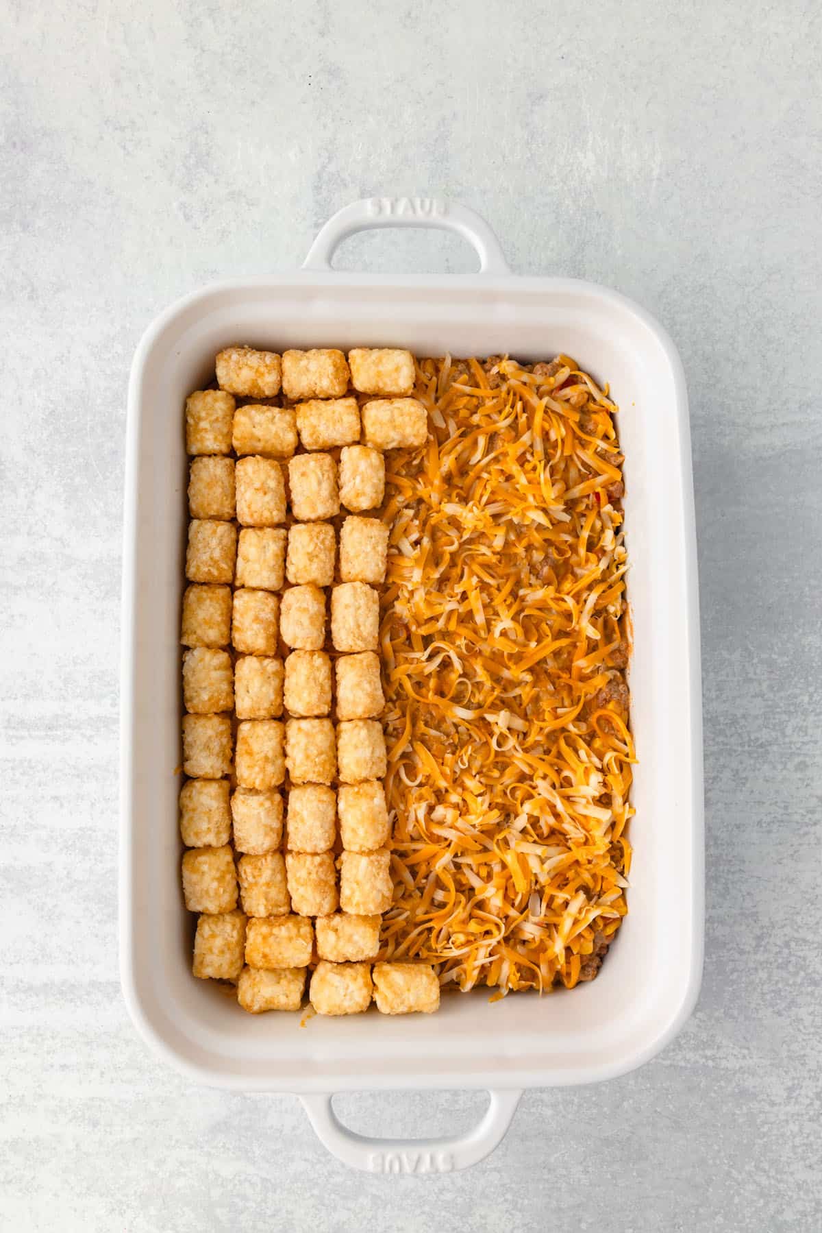 Arranging tater tots on top of a shredded cheese layer in a casserole dish.