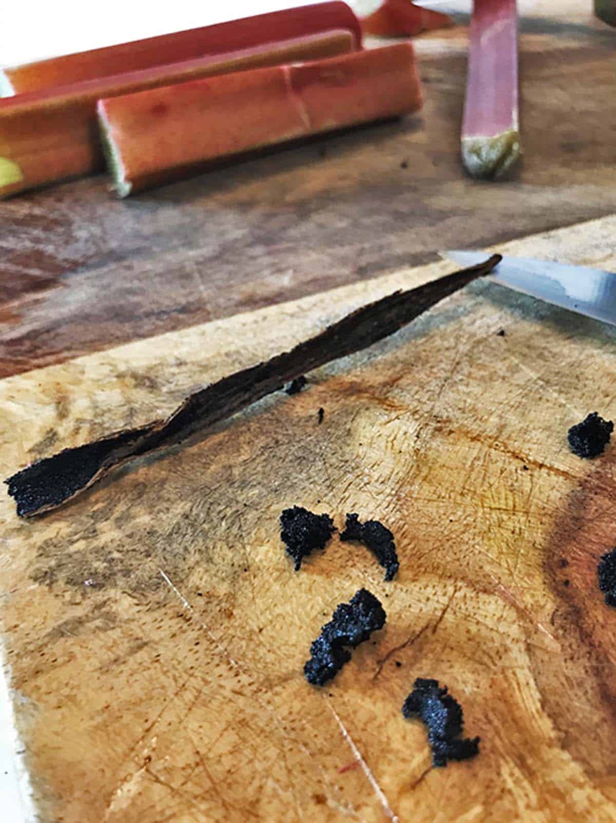 A vanilla pod slit in half with some vanilla beans spilled out onto a cutting board.