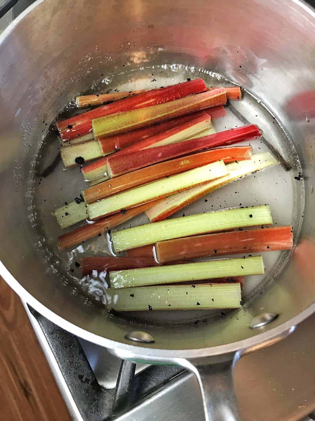 Some rhubarb stalks being poached in a sauce pan.