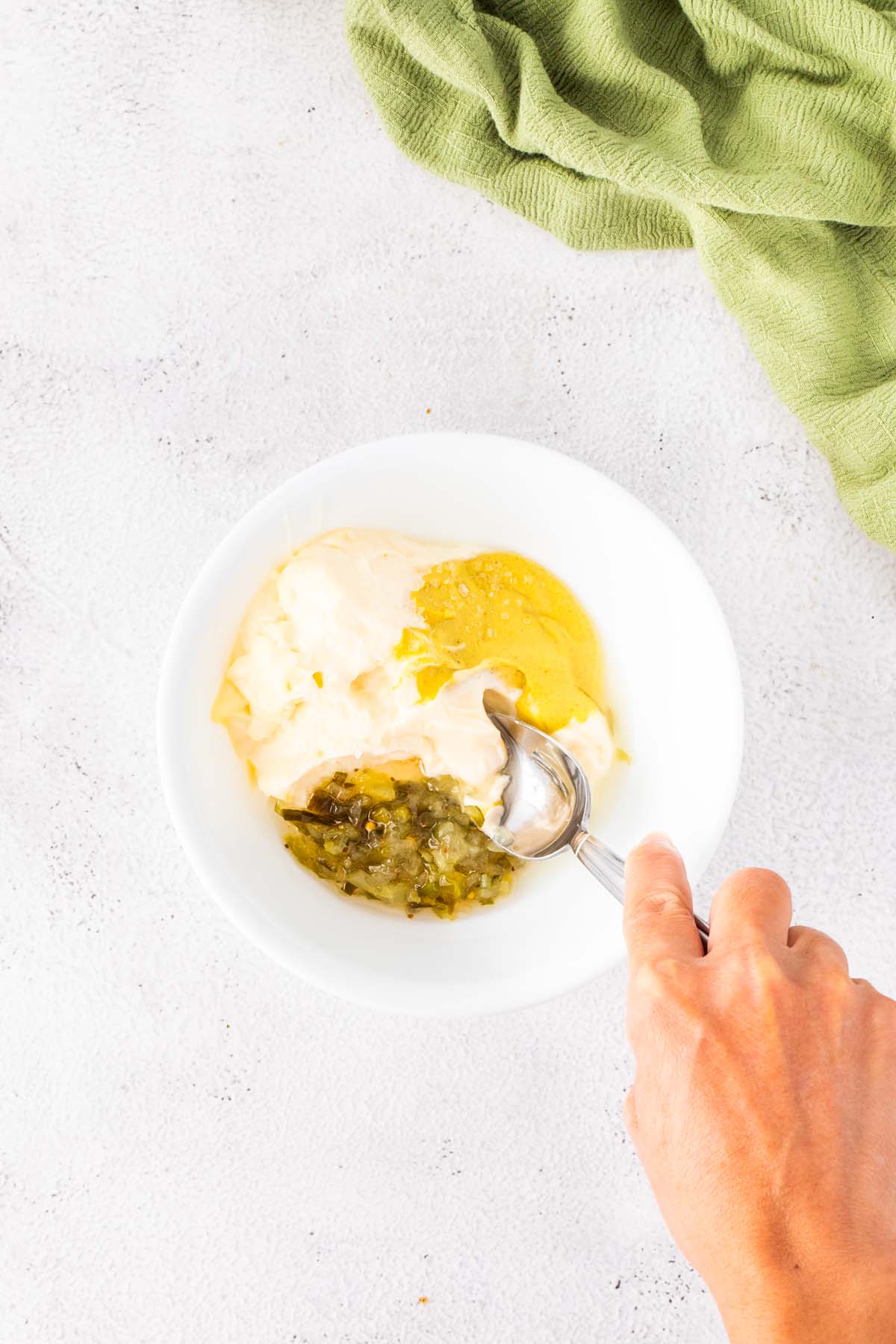 Stirring some mayonnaise, relish, and mustard in a small bowl.