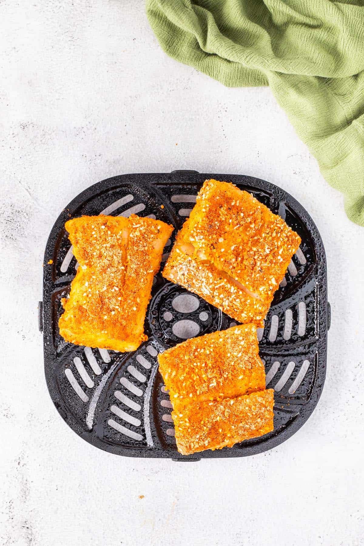 Three fish fillets in an air fryer basket.