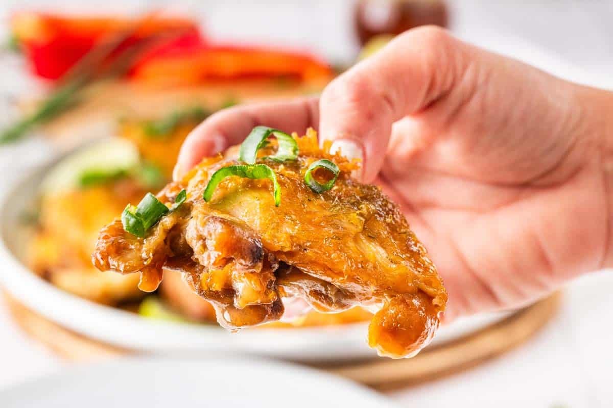 A person's hand, holding a crispy brown chicken thigh.