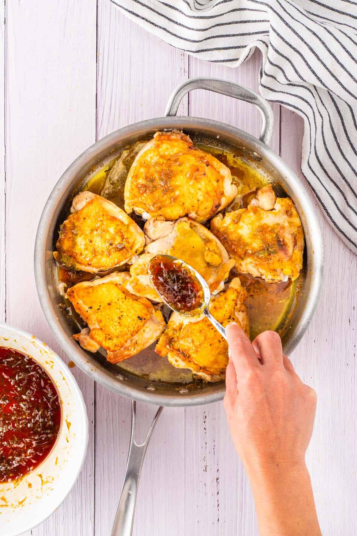Spooning sauce over the some chicken breasts in a pan.