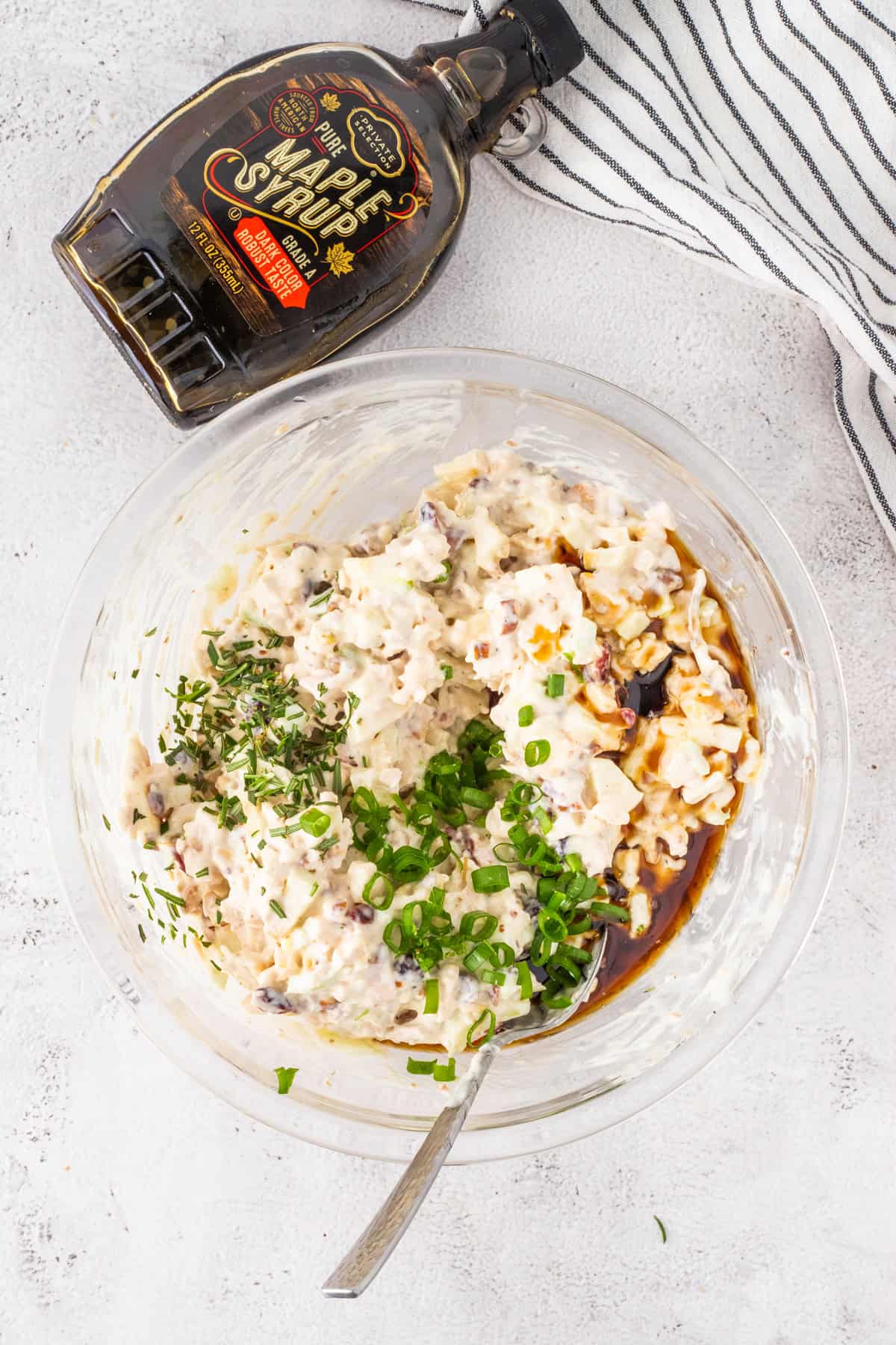 A bowl of chicken salad with some maple syrup and chopped green onions.
