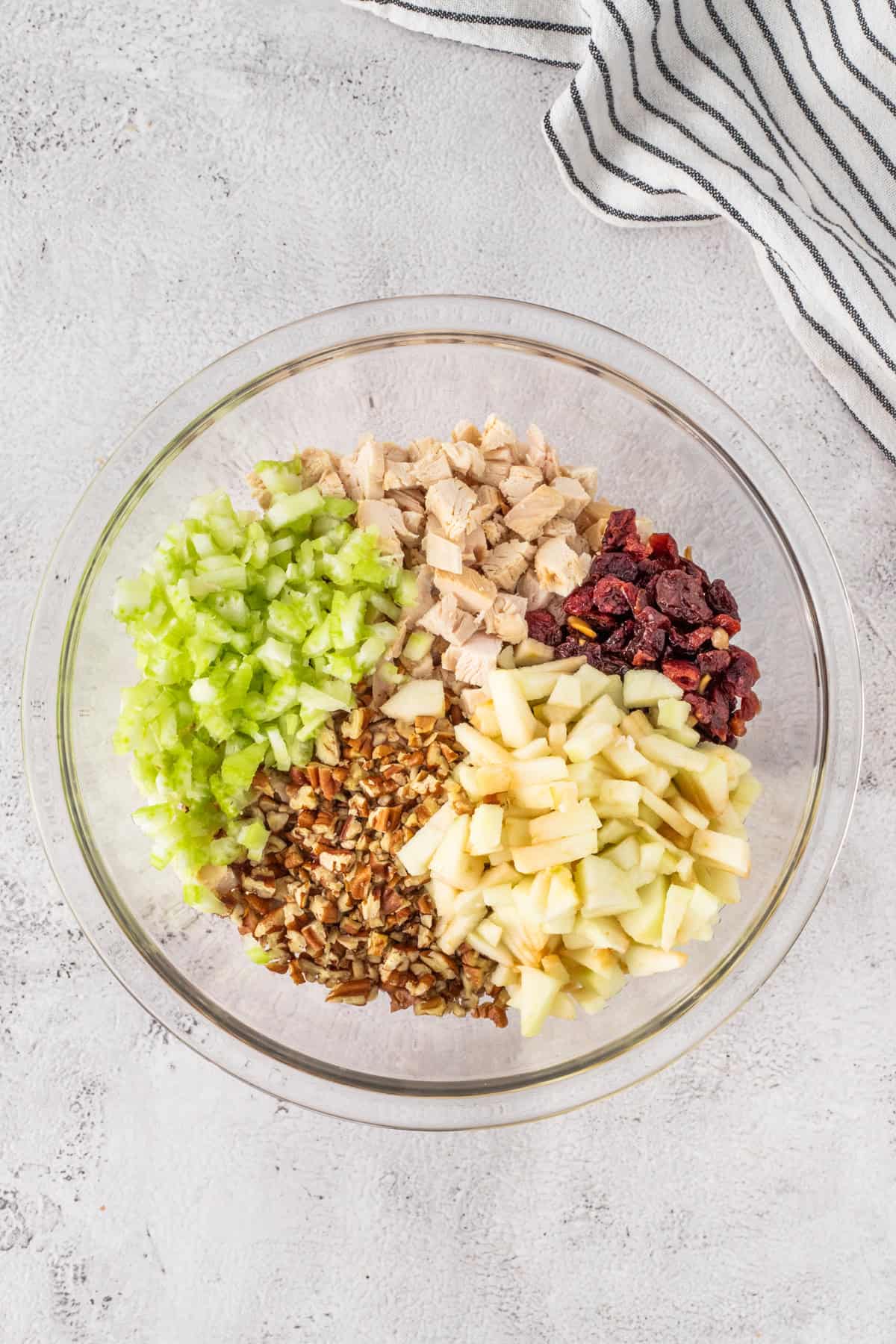 Some chopped up celery, pecans, chicken, and apples in a mixing bowl.