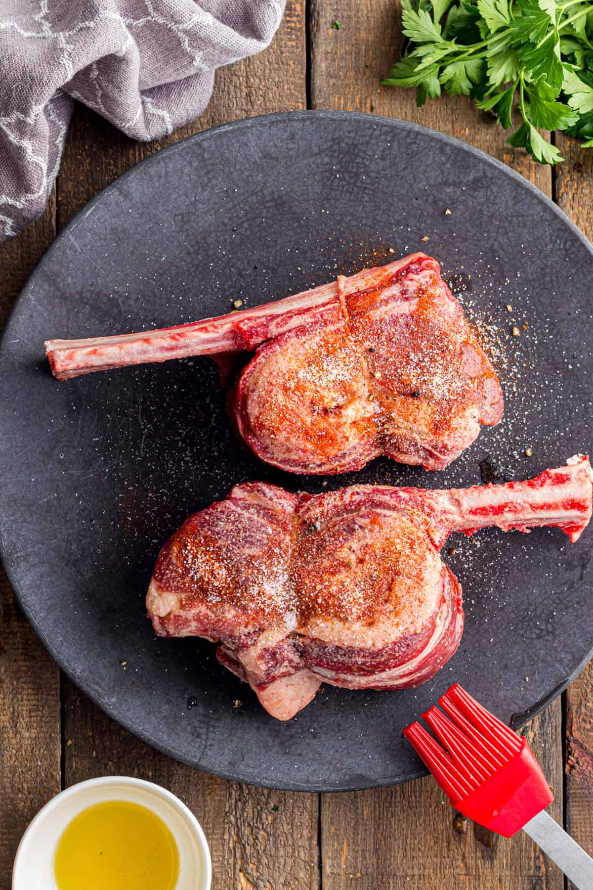 Some uncooked short ribs on a plate with seasoning sprinkled on them.