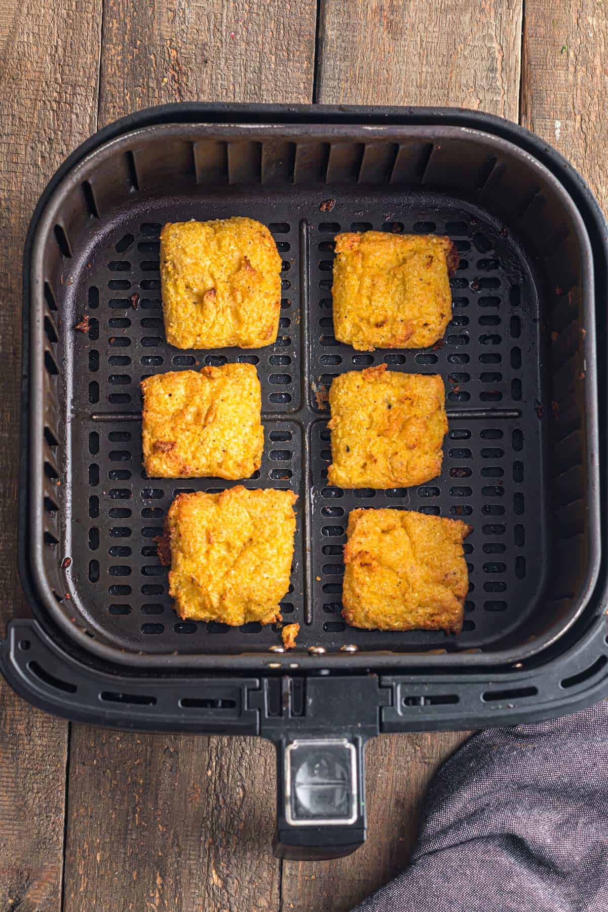 Some golden-brown homemade polenta in an air fryer basket.