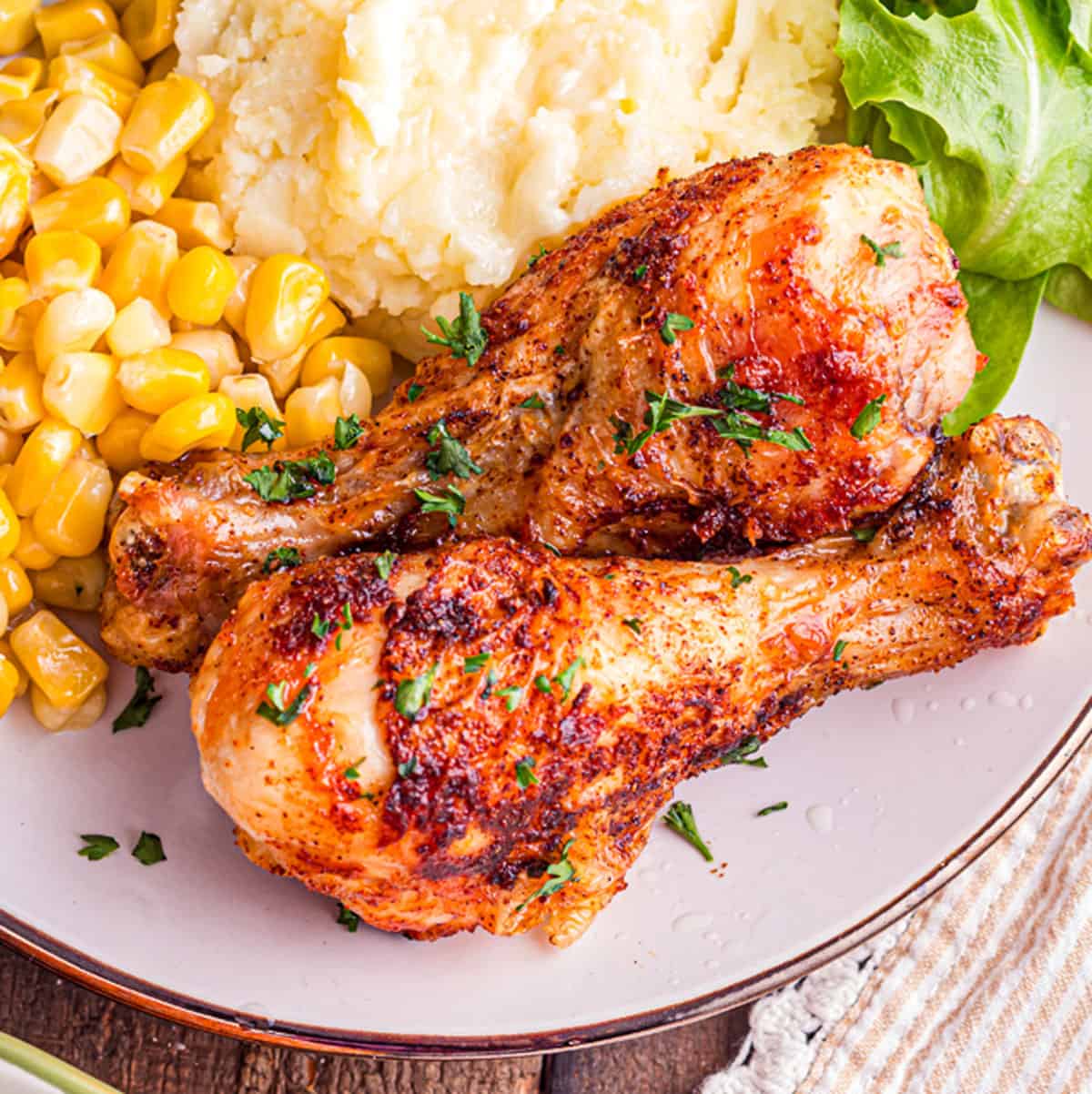A plate of crispy air fryer drumsticks with corn and mashed potatoes.