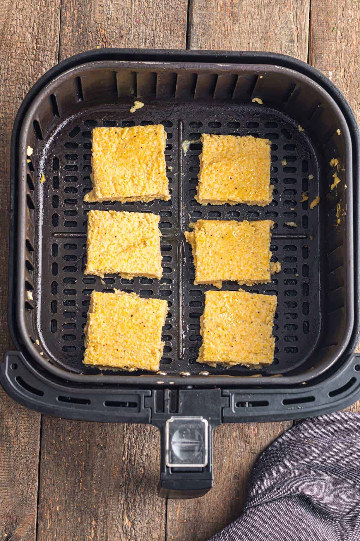 Six slices of homemade polenta in an air fryer basket.