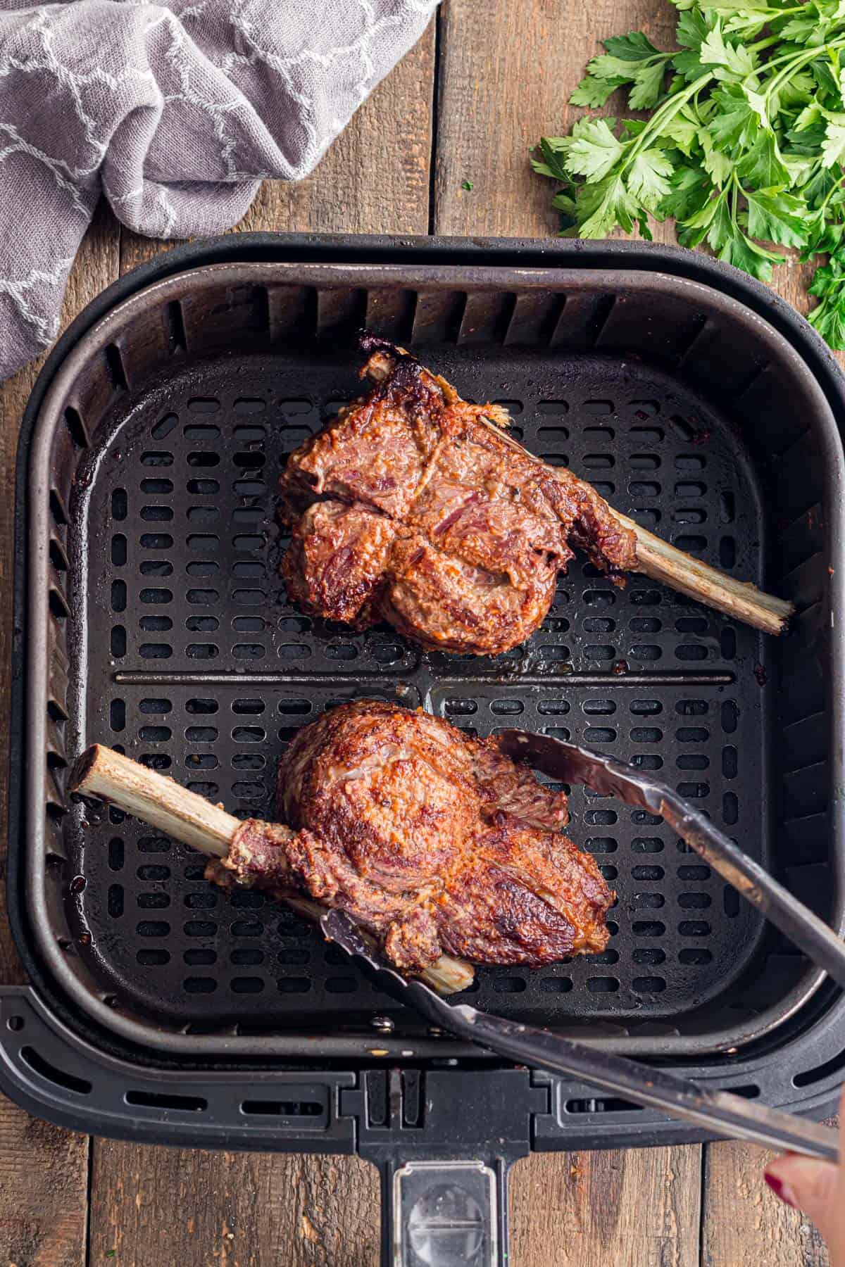 Using a set of tongs to turn short ribs in an air fryer.
