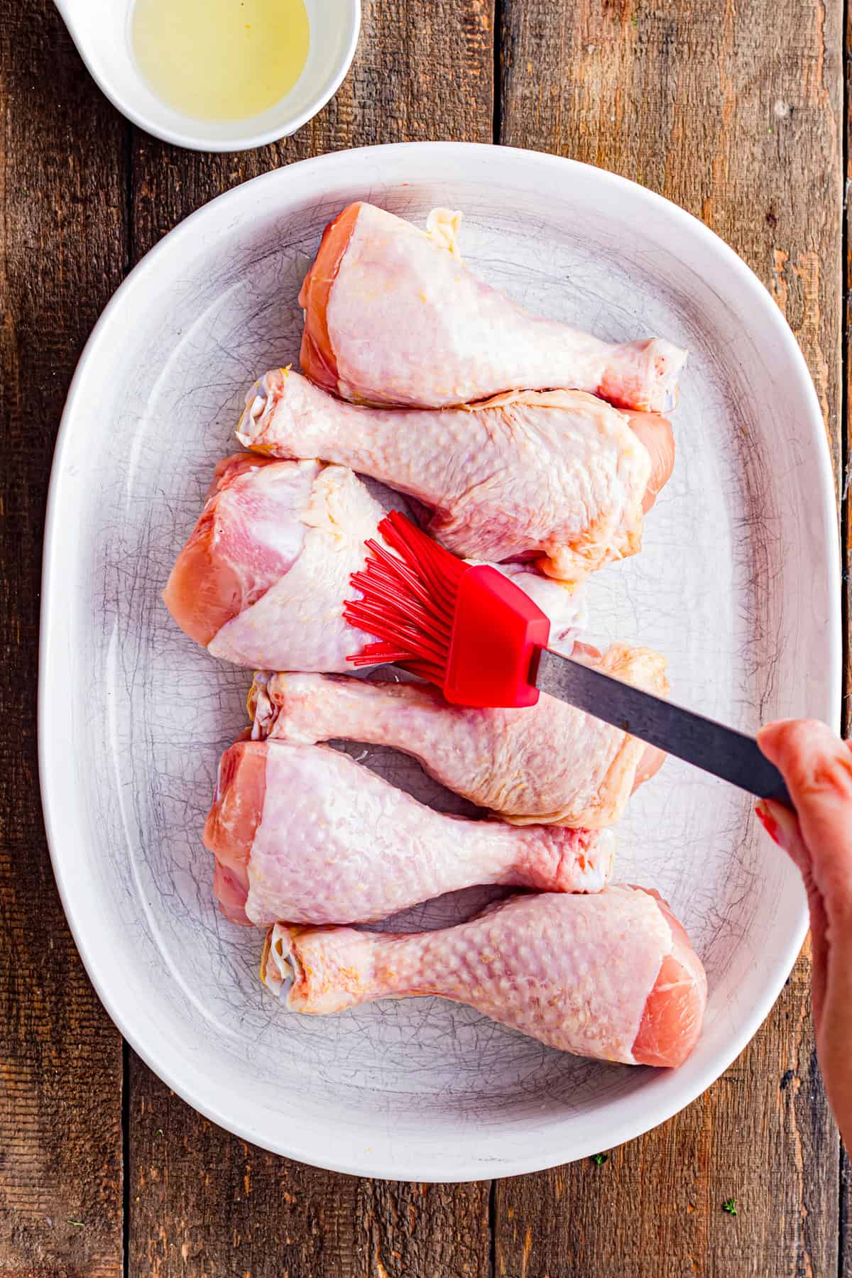 Brushing chicken drumsticks with olive oil.