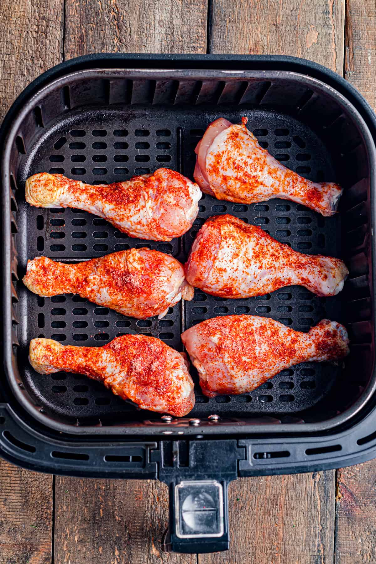 Some uncooked and seasoned chicken drumstick in an air fryer.