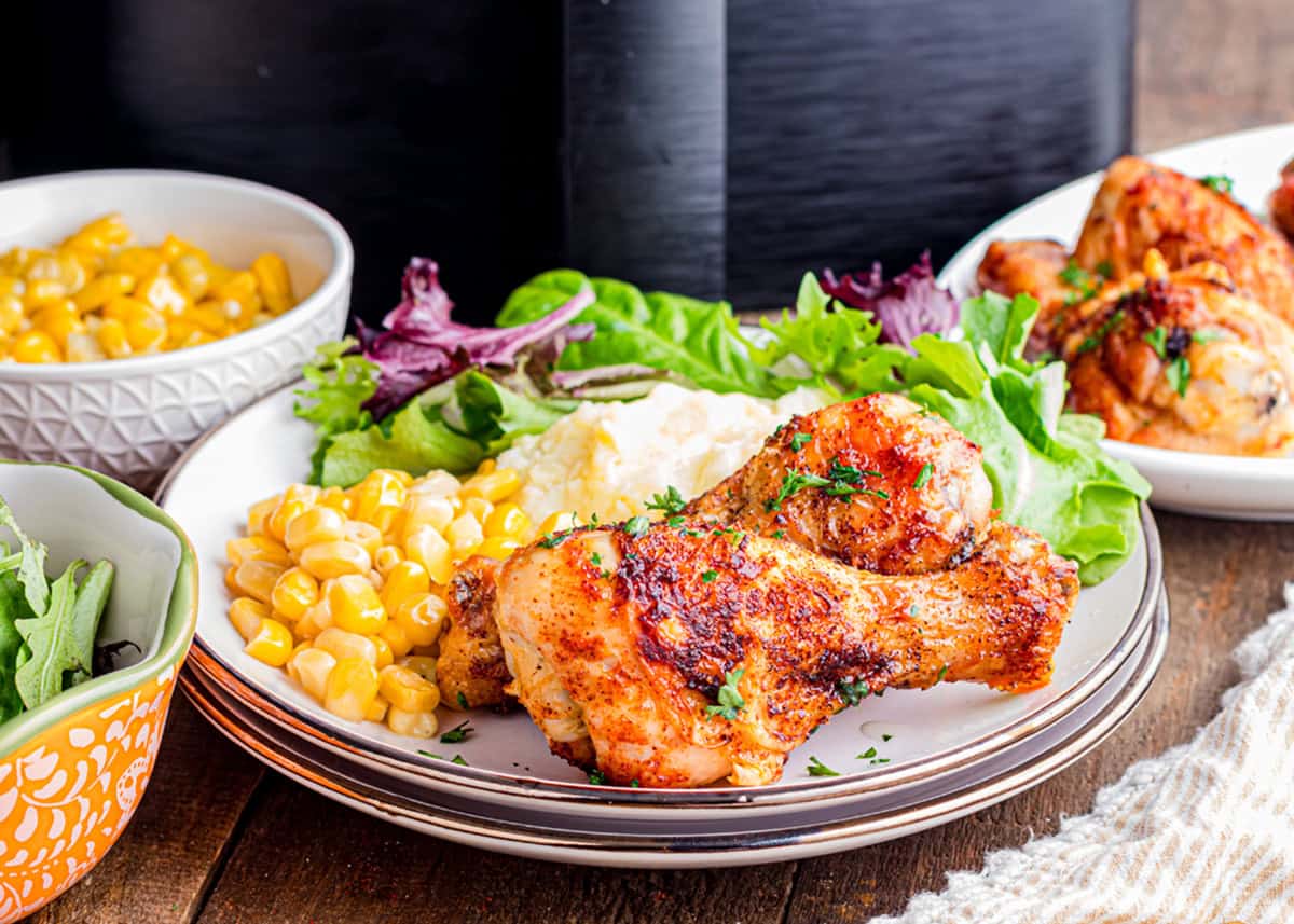 A dinner setting of air fryer drumsticks, corn, mashed potatoes, and salad.